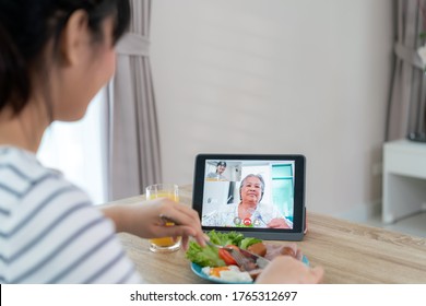 Asian Young Woman Virtual Happy Hour Meeting And Eating Food Online Together With Her Mother In Video Conference With Digital Tablet For A Online Meeting In Video Call For Social Distancing.
