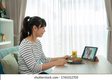 Asian Young Woman Virtual Happy Hour Meeting And Eating Food Online Together With Her Mother In Video Conference With Digital Tablet For A Online Meeting In Video Call For Social Distancing.
