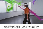 Asian young woman in virtual reality headset paints with wireless controllers, uses gestures to create abstract online artwork. Holographic 3D animation of paint drops. Augmented reality technology.