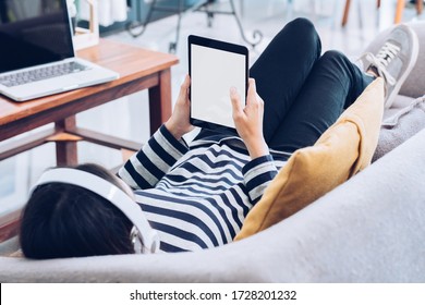 asian young woman watching tablet screen live streaming and wear headphone for listening sound lying down  on sofa at home - Powered by Shutterstock