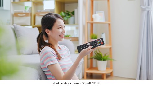 asian young woman is watching tv and sitting on the floor happily in living room at home - Shutterstock ID 2056878488