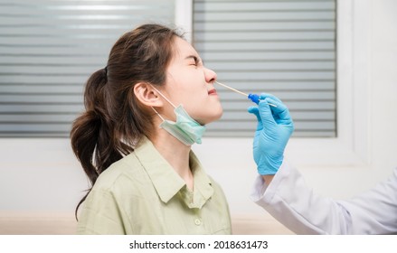 Asian Young Woman Wear Mask Sitting On Couch And Checked In Nasal Cavity Coronavirus From Doctor By Swab Method In Hospital. Medical Staff Taking Swab Nasal Mucus For Covid 19 Sample To Prevent Spread