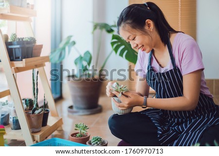 Asian young woman wearing apron caring for green indoor plant at home.New normal lifestyle concept of Hobby during quarantine and social distancing to stop spread disease of Coronavirus.