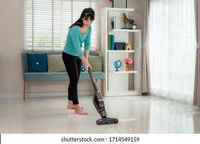 Asian Young Woman Wearing Casual Clothes  Is Cleaning House Floor In Living Room Using The Vacuum Cleaner At Home During Staying At Home Using Free Time About Their Daily Housekeeping Routine.