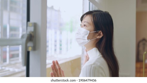 Asian Young Woman Wearing Face Mask Stay Isolation At Home For Self Quarantine Due To Epidemic Of COVID19 - She Looks Out The Window