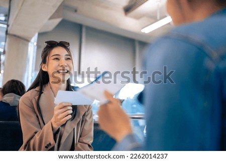 Asian young women talking together while waiting for airplane boarding. Attractive beautiful two girl friends feeling happy and relax, having fun communicating and discussing while sitting in airport.