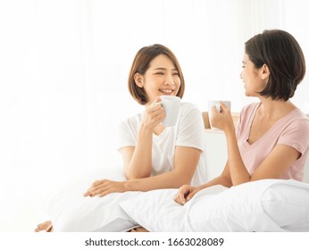 Asian Youth Teenager Two Girl Drink Morning Coffee, Tea Or Milk Warm Beverage While Talk Story Together And Start The Fresh New Day Of Energy Power On Bed With Sun Light In Bedroom At Friend's Home