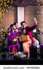 Asian/Indian Young Family Taking Selfie Or Self Photograph At Home With Gift Boxes On Diwali Festival Night.