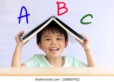 Asis Child Holds A Notebook Over His Head And Alphabet A B C.
Little Girl Asian Genius And  Eye Contact.
Concept Learn English Kids.British  