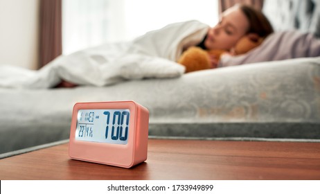 Asleep Caucasian Young Woman In The Background With Digital Alarm Clock In Focus. Selective Focus. Horizontal Shot