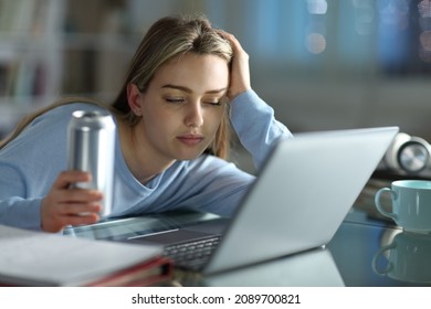 Asleep student trying to study with a laptop holding energy drink in the night at home