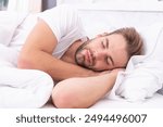 Asleep young man sleeping. Resting peacefully in comfortable bed. Deep male sleep. Man sleeping at night. Sleepy man lying on bed sleeping at white bedroom. Serene sleep environment