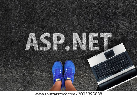 asp.net programming language. Legs in sneakers standing next to laptop and word asp.net 