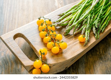 asparagus and a branch with yellow cherry tomatoes on a wooden board. - Powered by Shutterstock