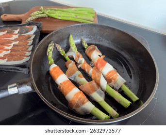 Espárragos envueltos en jamón y queso fritos en una sartén de hierro fundido - preparación casera de aperitivos