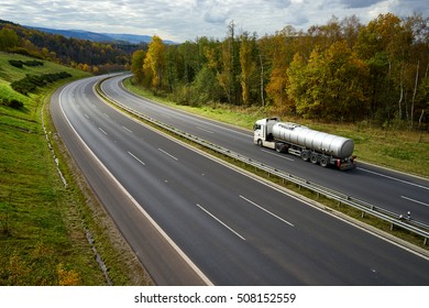 Asphalt highway with driving a silver tanker in the autumn landscape.