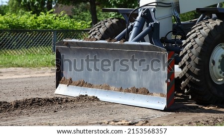 Asphalt laying in village, industrial machinery - heavy bulldozer scoop blade levels asphalt surface at dry summer day. Rebuilding of the road