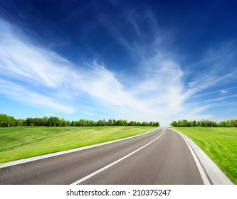 Asphalt Road Between Grassy Meadow With Trees On Horizon. Summer Landscape With Blue Sky