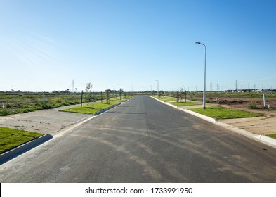 Asphalt road between vacant lands in a new residential suburb. Tarneit, Melbourne, VIC Australia. Concept of real estate development, housing, urbanization, and land for sale.