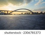 Asphalt road and bridge with city skyline at sunset