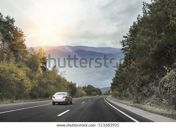 Asphalt road and cars in the mountains with\
cloudy sky on the\
background.