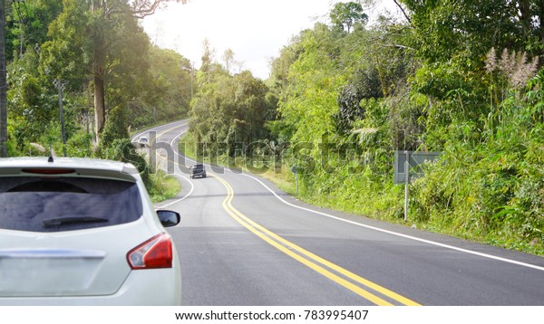 Asphalt road with cars passing through the forest\
in north of Thailand and sunshine morning. Vacation and travel\
concepts.Soft focus