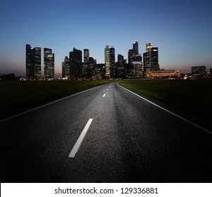 Asphalt Road And City With Illuminated Buildings On The Horizon