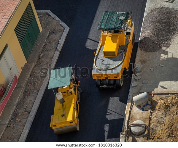 Asphalt road construction site with paving machine\
compacting asphalt. Pneumatic Tire Roller and Steel Wheel Roller at\
work.  View from above.