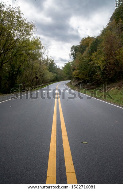 asphalt road with a dividing strip in a\
forested mountainous area in cloudy weather in\
autumn
