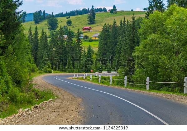 asphalt road with a\
dividing strip going between green trees against a background of a\
slope with houses