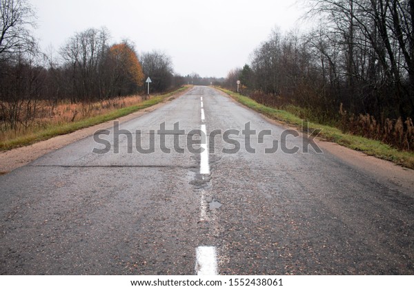 Asphalt road with a dividing strip. Gray autumn\
roadsides. Overcast.