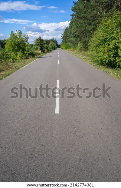 An asphalt road with a dividing strip of road\
markings passes through the\
forest.