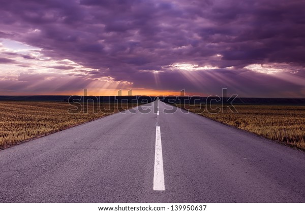 Asphalt road in the\
fields before the storm