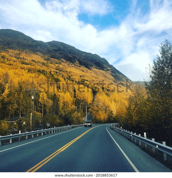 An asphalt road at the foot of a mountain with\
yellow autumn trees