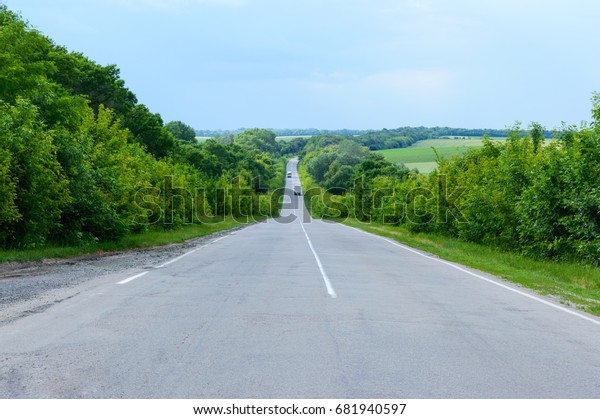 Asphalt road, goes into the distance. Green trees\
are on both sides.