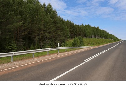 An asphalt road going uphill. Dense coniferous-deciduous forest on the side of the highway. Movement up the slope.