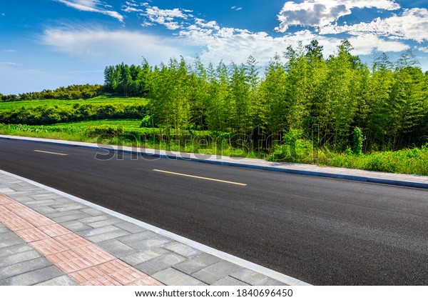 Asphalt road and green plants with mountain\
natural scenery in Hangzhou on a sunny\
day.