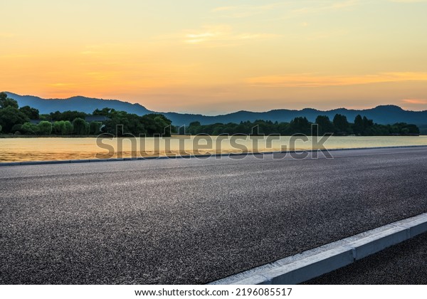 Asphalt road and lake with mountain nature\
background at sunset
