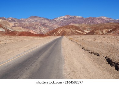 Asphalt Road Leading Through Steaming Hot Landscape Of Death Valley National Park, California, USA. Super Hot Sunny Day In The Desert Of The Southwest. Vast Land Of Dirt And Dust.