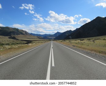 an asphalt road with road markings runs among the mountains under a blue sky with white clouds on a sunny autumn day - Shutterstock ID 2057744852