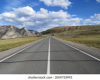 An Asphalt Road With Road Markings Runs Among The Mountains Under A Blue Sky With White Clouds On A Sunny Autumn Day