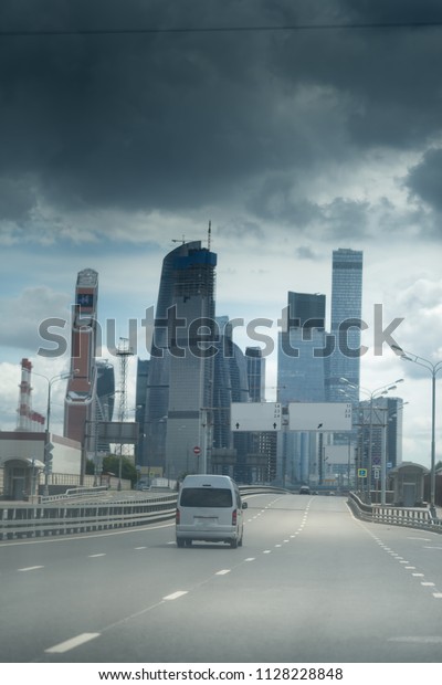 Asphalt road\
to the modern city. Dark stormy\
clouds.