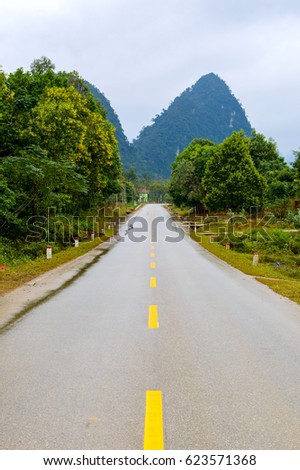 Asphalt Road in mountain area with yellow line in the middle of the road for road background or business concept. Thunder clouds in the sky.
