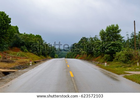 Asphalt Road in mountain area with yellow line in the middle of the road for road background or business concept. Thunder clouds in the sky.