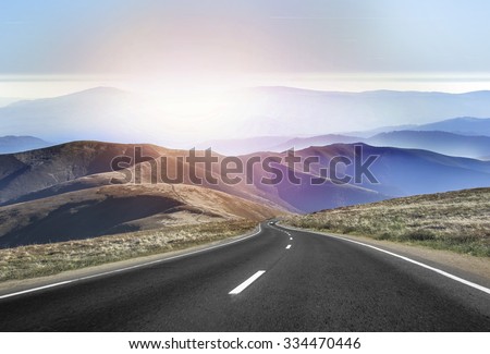 Asphalt road in the mountains with soft sky on the background.