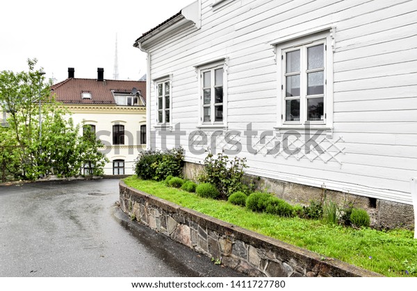 Asphalt\
road on the side of the house in the Arendal City house with the\
green bush and green grass on the side of the house on the flower\
pot at Norway. Spring time in the raining day. \
