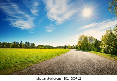 asphalt road panorama in countryside on sunny spring day.. Route in beautiful nature landscape with sun, blue sky, green grass and dandelions - Shutterstock ID 1014303712