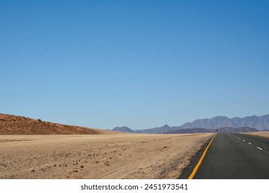 Asphalt road in perspective in desert under clear blue sky. The road leads to distant mountains and hills - Powered by Shutterstock