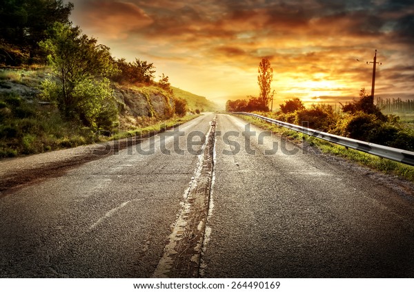 Asphalt road receding into the distance under a\
dramatic sky of fire