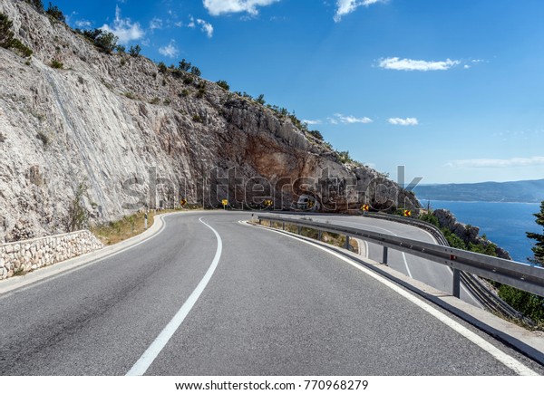 Asphalt road\
to the sea. Asphalt highway in a sunny day outside the city passing\
through the cliff next to the\
sea.